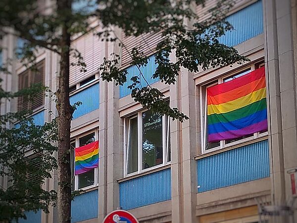 Das Bild zeigt zwei Regenbogenflaggen an den Fenstern des Büros des StudierendenRates