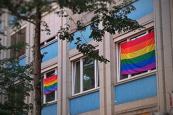 Das Bild zeigt zwei Regenbogenflaggen an den Fenstern des Büros des StudierendenRates