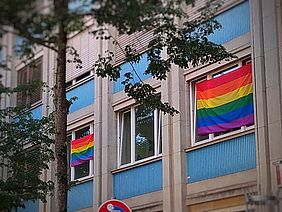 Das Bild zeigt zwei Regenbogenflaggen an den Fenstern des Büros des StudierendenRates