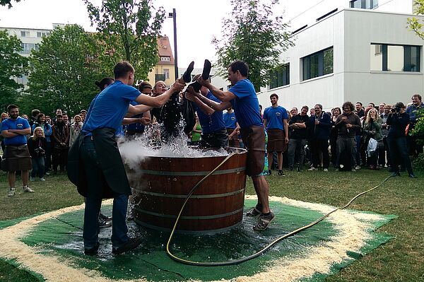 Menschen heben Person aus Wasserbottich heraus bei einem Fest im Freien