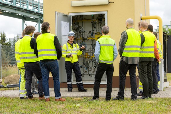 Austausch im Wasserstoffdorf 8 Männer unterhalten sich vor einer Gasregelanlage