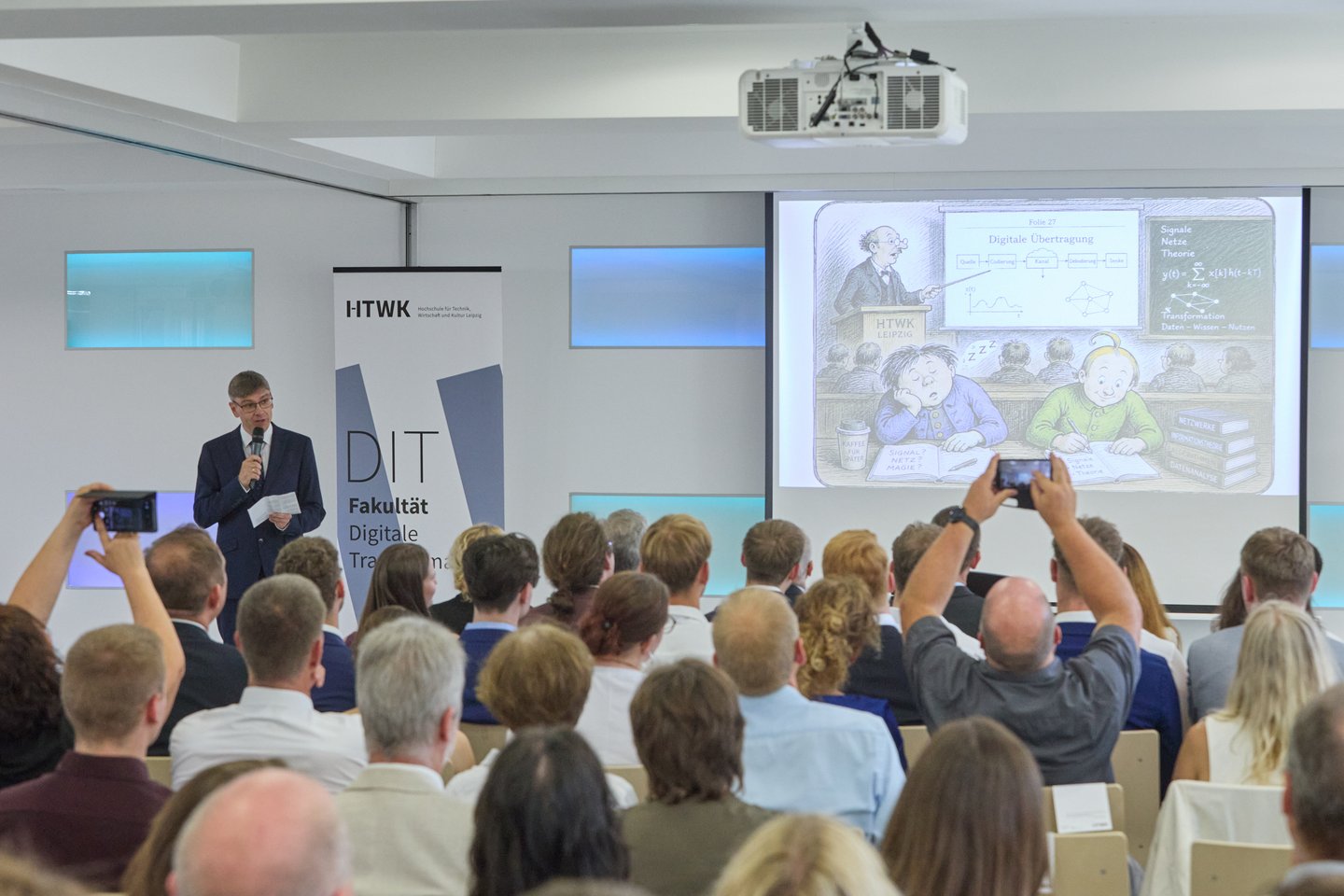 Prof. Andreas Thor Redner mit Mikro und Präsentation vor vollbesetzten Stuhlreihen