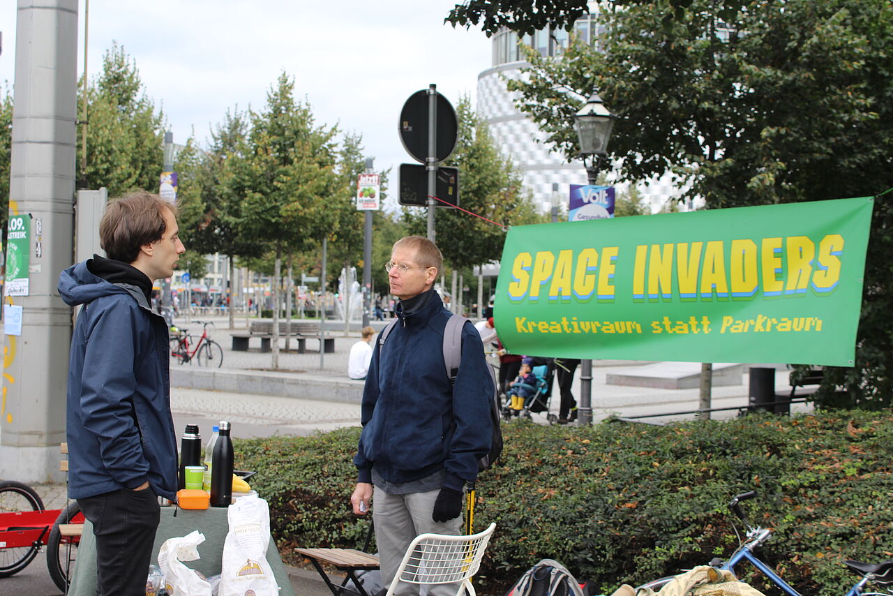 Zwei Menschen unterhalten sich vor dem "Space Invaders" Plakat