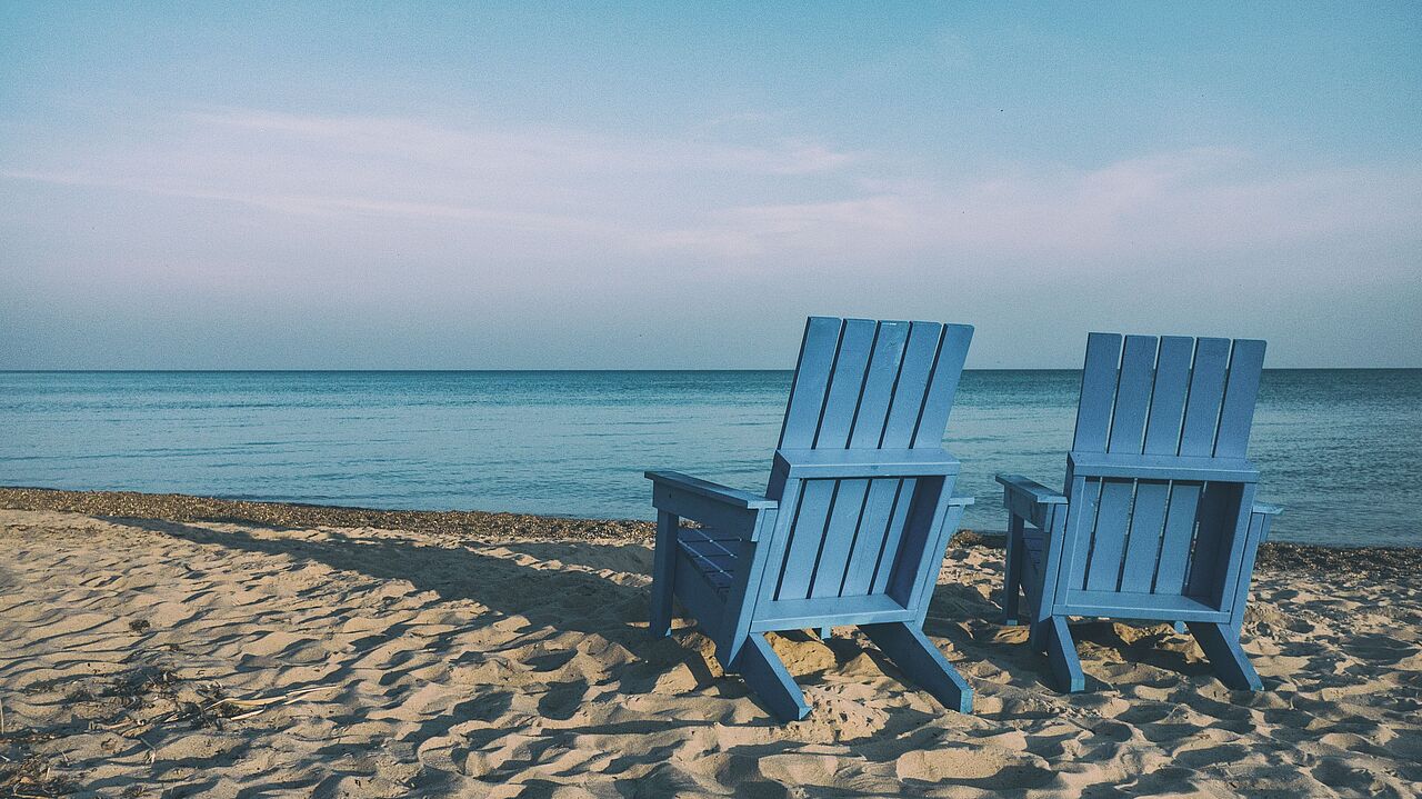 Zwei blaue Liegestühle stehen am Strand mit Blick auf das Meer