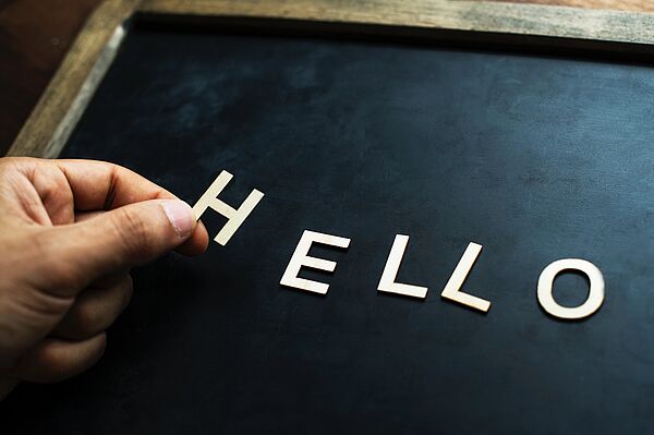 Eine Person legt das Wort „Hello” mit Papierbuchstaben auf einer Tafel