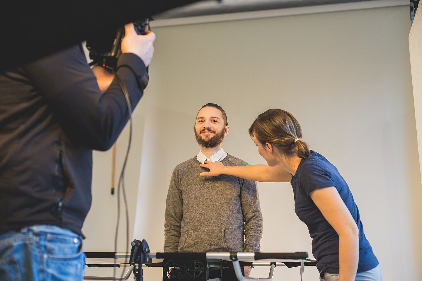 Wladimir Sawin beim Shooting in Berlin. (Foto: familie redlich AG/Niklas Schader) Wladimir Sawin wird vor grauer Fotowand von einer Maskenbildnerin für das Shooting vorbereitet, indem sie sein Hemd richtet.