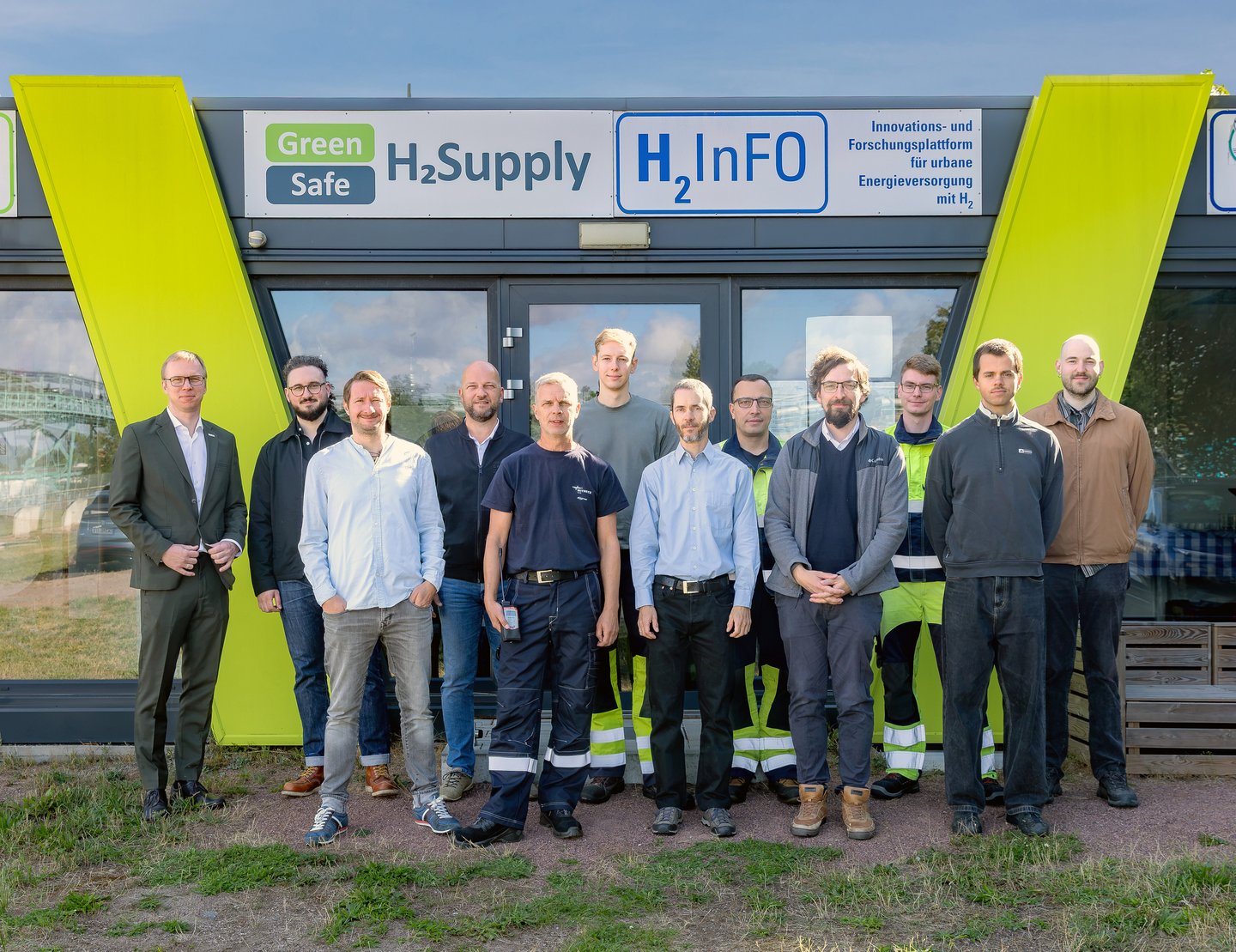 Gruppenbild im Wasserstoffdorf Bitterfeld-Wolfen 12 Männer stehen zum Gruppenbild vor einem Pavillon