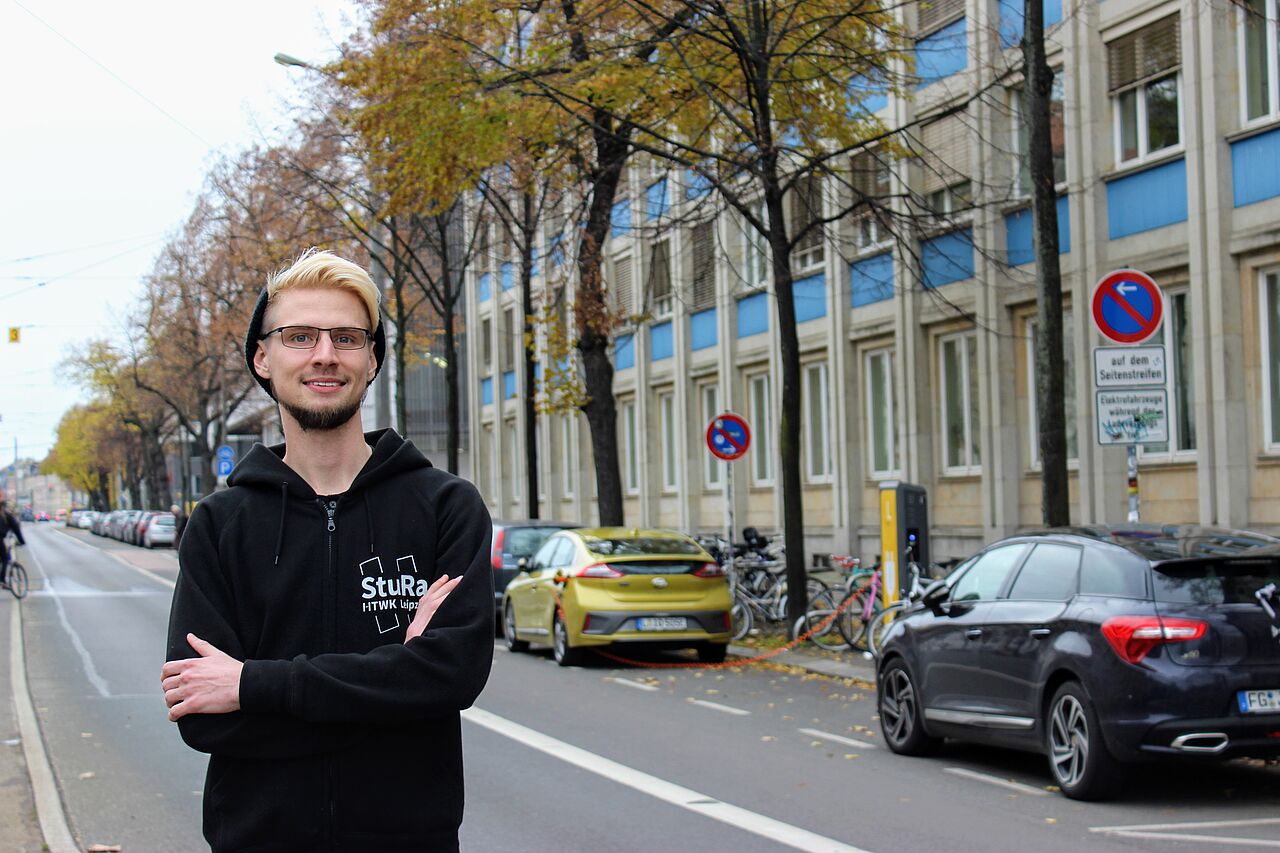 Paul Hösler, Kandidat für die Wahl zum Hochschulrat an der HTWK Leipzig, steht lächelnd mit verschränkten Armen auf der Karl-Liebknecht-Straße vor dem Geutebrück-Bau